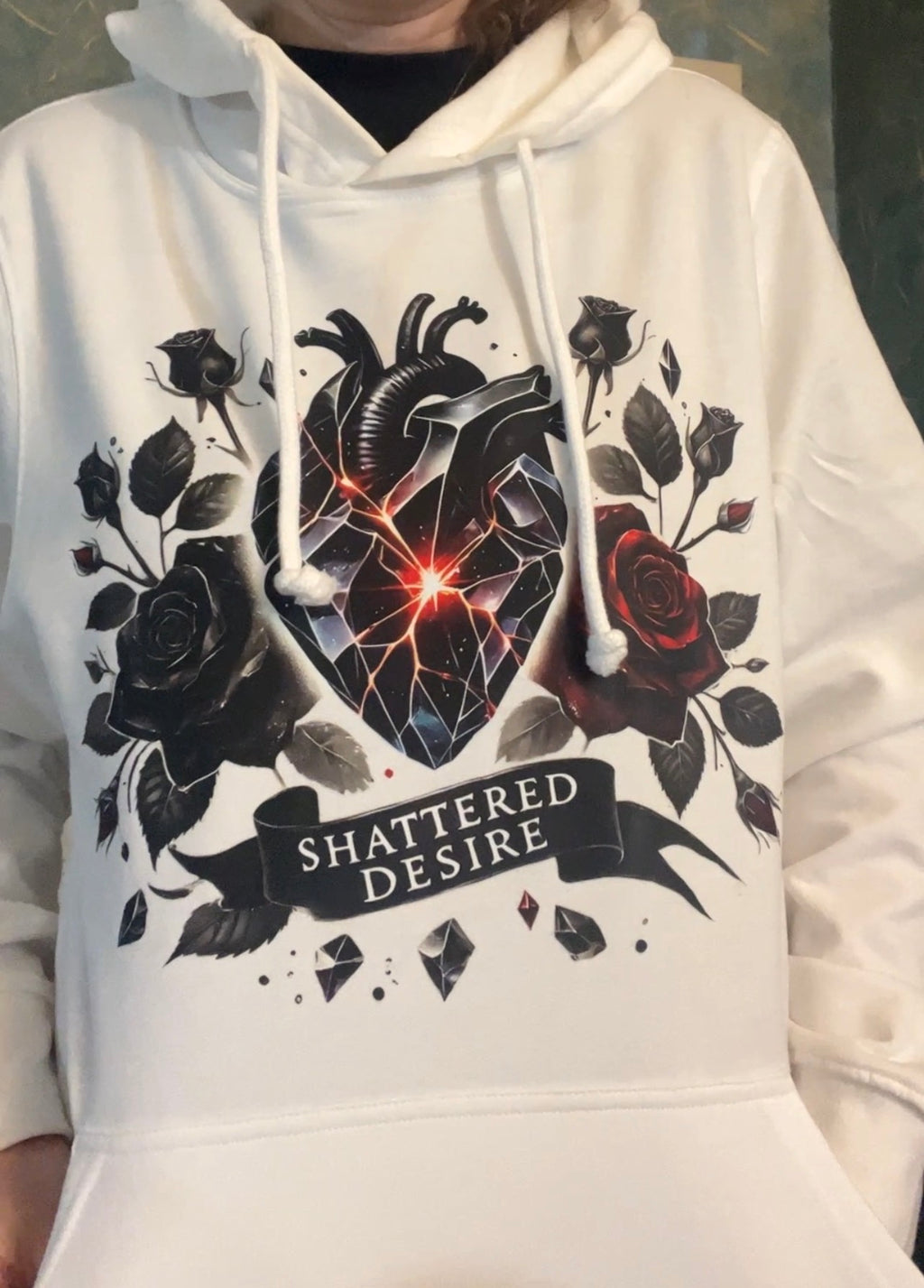 White hoodie featuring a gothic shattered anatomical heart with glowing cracks, surrounded by black and red roses, and the text “Shattered Desire” printed across the front.